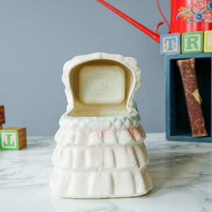 May include: White ceramic baby crib planter with a pink and blue floral design. The crib is open and the inside is empty.