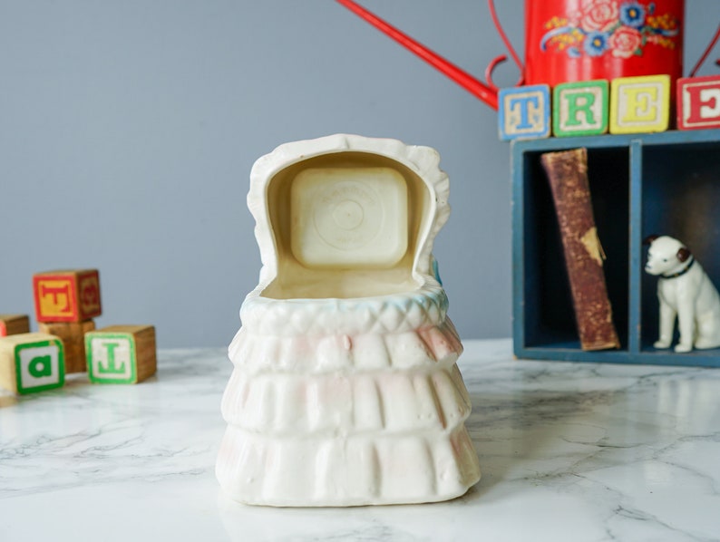 May include: White ceramic baby crib planter with a pink and blue floral design. The crib is open and the inside is empty.