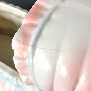May include: A white ceramic baby carriage cookie jar with a pink and blue trim. The lid is open and the inside of the jar is visible.