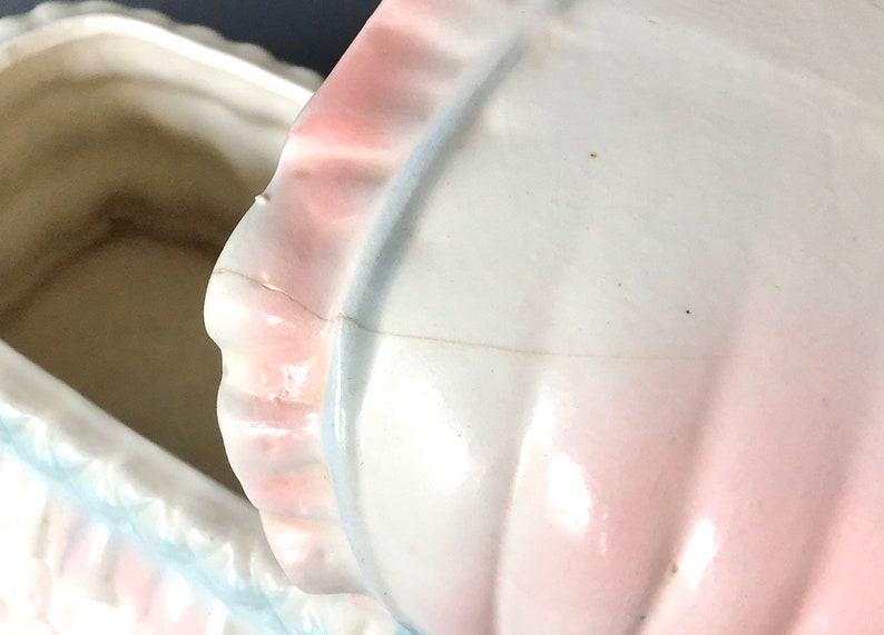 May include: A white ceramic baby carriage cookie jar with a pink and blue trim. The lid is open and the inside of the jar is visible.