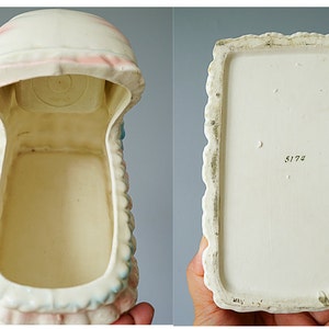 May include: White ceramic baby crib planter with pink and blue accents. The planter is empty and has a number "5173" on the bottom.