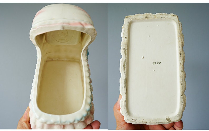 May include: White ceramic baby crib planter with pink and blue accents. The planter is empty and has a number "5173" on the bottom.