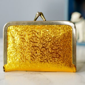 Puede incluir: Una peque&ntilde;a cartera de monedas de oro con un marco de plata y un dise&ntilde;o en relieve floral.