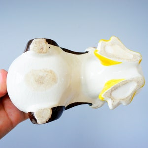 May include: White ceramic planter shaped like a dog with brown and yellow accents. The planter is lying on its side, showing the bottom of the planter.