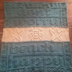 May include: A crocheted baby blanket with a blue and white color scheme. The blanket features the words "Welcome Home" and a design of two stars.
