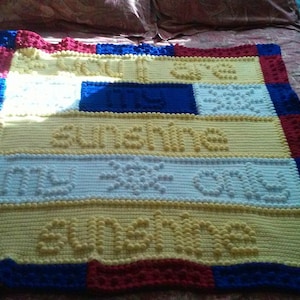 May include: Handmade crochet blanket in yellow, white, blue, and red. The blanket features the words "You are my sunshine, my only sunshine" in raised letters. The blanket is rectangular and has a colorful border.