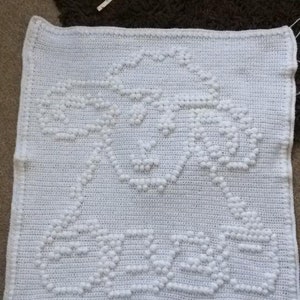 May include: White crocheted baby blanket featuring a raised sheep design. The blanket is made with white yarn and has a textured surface.