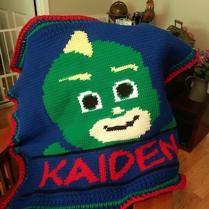 May include: A blue, green, red and white crocheted blanket featuring a cartoon character's face and the name "KAIDEN" in red letters.