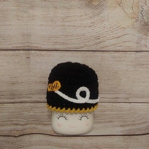 May include: Black crocheted hat with white and yellow trim. The hat has a white band with a swirl design.