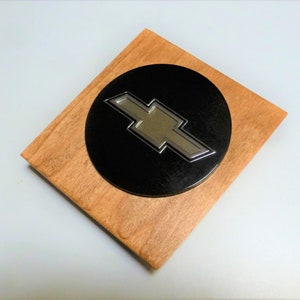 May include: A wooden plaque with a black circle in the center. The circle has a silver Chevrolet logo on it.