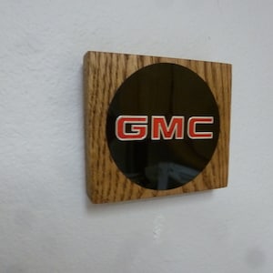 May include: A wooden plaque with a black circle and the red text "GMC" in the center.