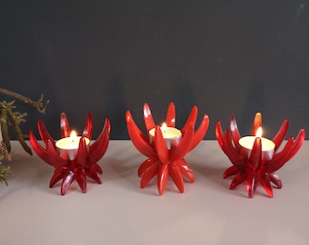 Może przedstawiać: Trzy czerwone świeczniki w kształcie stylizowanych kwiatów z pojedynczą świeczką typu tealight w każdym.
