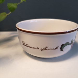 Może przedstawiać: Biała ceramiczna miska z brązową krawędzią i kwiatowym wzorem. Miska ma napis "Pulmonaria officinalis" nadrukowany na boku.