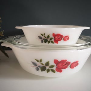 Op de afbeelding: Twee witte Pyrex bakschalen met een bloemenmotief met rode rozen en groene bladeren. De schalen zijn in elkaar geschoven.