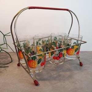 May include: A vintage six-glass set with a metal carrier. The clear glasses feature a colourful fruit design with cherries, apples, and lemons. The carrier has a red handle and feet, and a chrome finish.