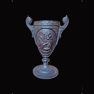 May include: An intricately carved, dark blue chalice with a detailed relief depicting figures. The chalice features two decorative handles and a circular base. The background is black.