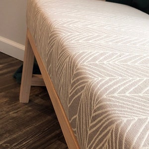 May include: A light brown wooden bench with a white and gray chevron patterned cushion.