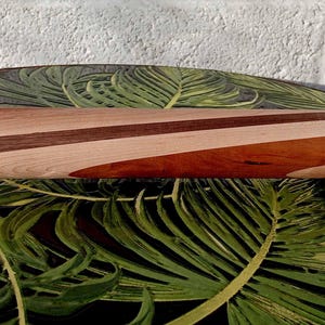 May include: A wooden rolling pin with alternating light and dark wood stripes. The rolling pin has a cylindrical body and rounded handles. The design features a mix of light and dark brown wood tones, creating a visually appealing pattern. The rolling pin is designed for kitchen use.