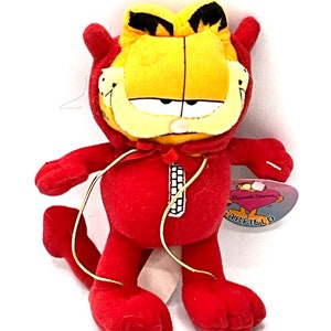 May include: Red plush Garfield toy wearing a devil costume with a gold zipper and tail. The toy has a tag that says "Russell Stover Garfield".