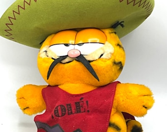 May include: A plush orange Garfield cat wearing a green sombrero and a red poncho with the word "¡OLÉ!" printed on it.