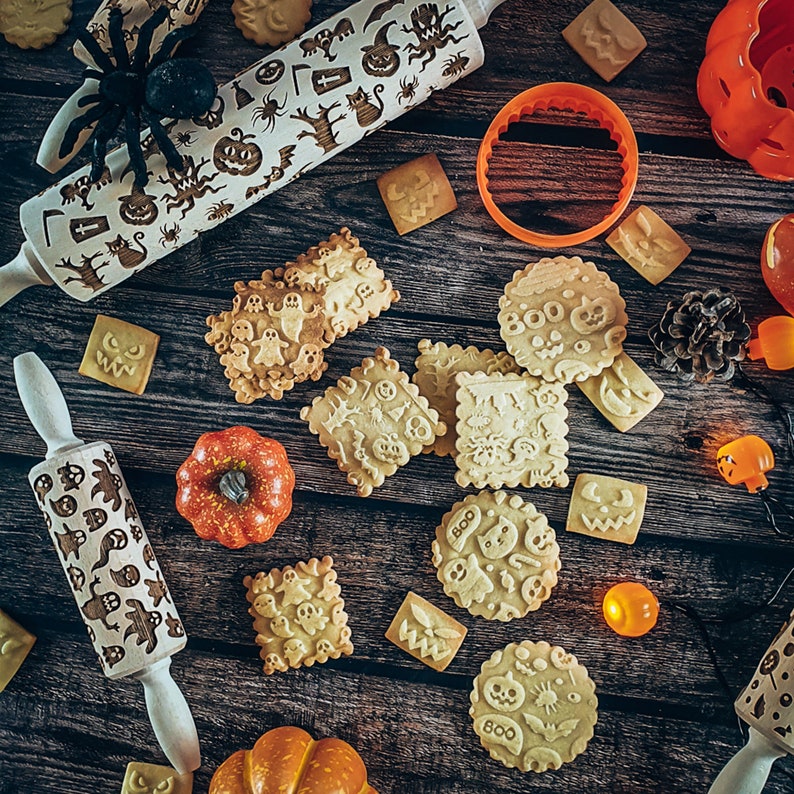 Peut inclure: Gros plan sur une table en bois avec divers biscuits et rouleaux &agrave; p&acirc;tisserie sur le th&egrave;me d'Halloween. Les biscuits sont d&eacute;cor&eacute;s de visages effrayants, de fant&ocirc;mes et du mot "BOO". Les rouleaux &agrave; p&acirc;tisserie sont grav&eacute;s de motifs d'Halloween.