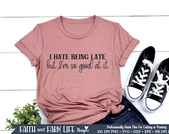 以下が含まれることがあります： ピンクのTシャツに「I HATE BEING LATE but I'm so good at it」という文字がプリントされています。Tシャツは白い表面に置かれ、背景には黒いスニーカーと植物があります。