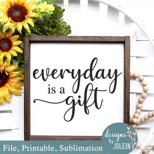 May include: A white sign with a wood frame and the text "everyday is a gift" in black cursive font. The sign is decorated with sunflowers and wooden beads.