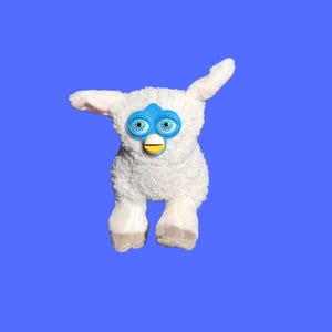 Puede incluir: Un juguete de peluche blanco con detalles azules y amarillos, con ojos grandes y expresivos. El juguete tiene una textura suave y un diseño distintivo, con una placa frontal azul y una característica en forma de pico amarillo. El fondo es azul liso.