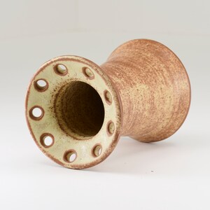 May include: A brown and beige ceramic vase with a flared opening and a ring of holes around the top.