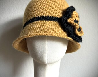 May include: A crocheted cloche hat in a mustard yellow color with a black crocheted flower accent.