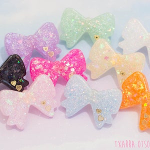 May include: Assortment of colorful glitter resin bows with gold heart accents. The bows are in various colors including pink, purple, blue, green, orange, and black.