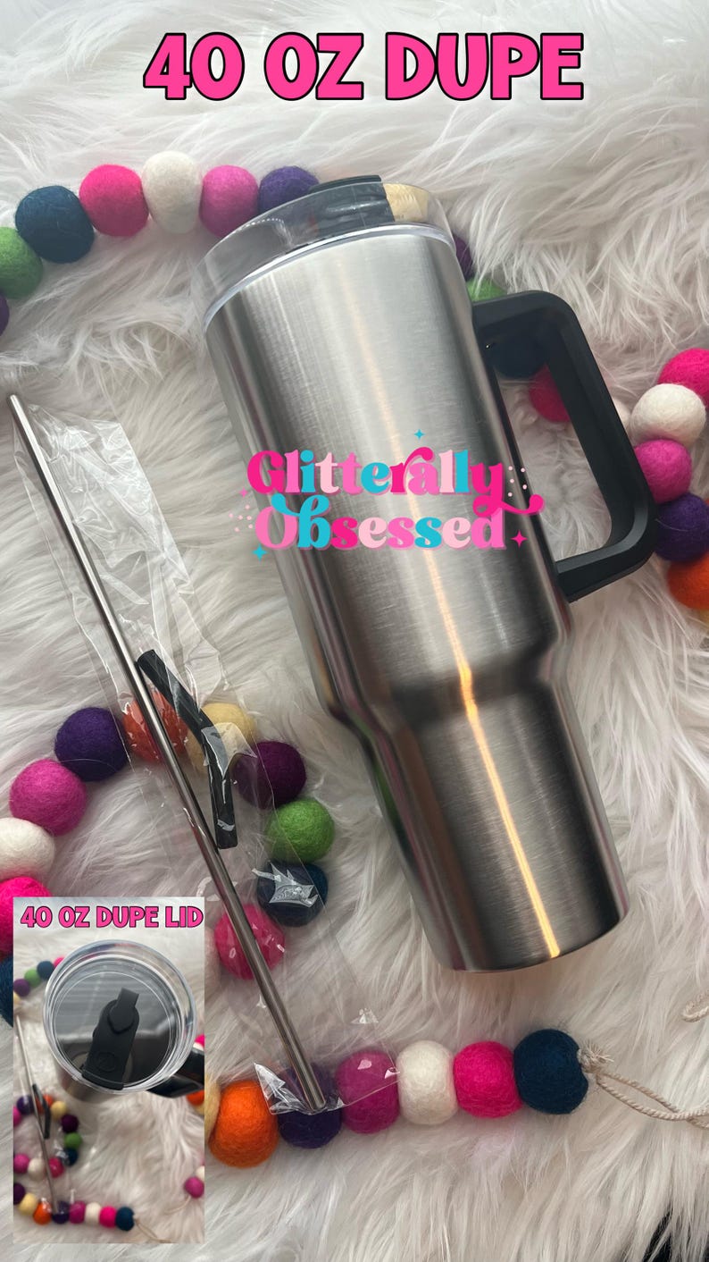 May include: A stainless steel 40 oz tumbler with a black handle and lid, accompanied by a metal straw and a lid. The text "40 OZ DUPE" and "Glitterally Obsessed" are visible. Colorful felt ball garland decorates the scene.