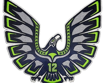 Puede incluir: Un parche bordado azul y verde con un águila estilizada con las alas extendidas. El águila tiene un pico verde y ojos amarillos. El número "12" está centrado en el pecho del águila.