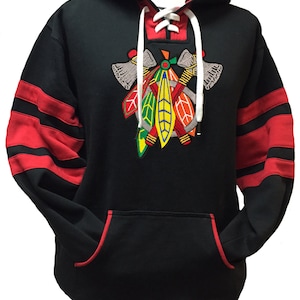 May include: Black hoodie with red and black striped sleeves. The hoodie has a drawstring hood and a lace-up neckline. The front of the hoodie features an embroidered logo of a Native American headdress with crossed tomahawks.