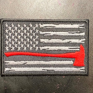 May include: A black and white embroidered American flag patch with a red line and a red axe. The flag is distressed and has a worn look.