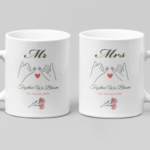 Pode incluir: Duas canecas de cerâmica branca com alças, cada uma com um design para um casal. Uma caneca diz "Mr" e a outra "Mrs". Ambas as canecas têm um gráfico de promessa mindinho, um coração vermelho e o texto "Together We Bloom Est. January 2025".