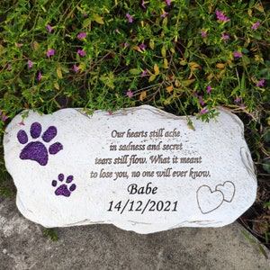 May include: A white stone memorial with purple glitter paw prints and the name "Babe" and date "14/12/2021". The inscription reads "Our hearts still ache in sadness and secret tears still flow. What it meant to lose you, no one will ever know."