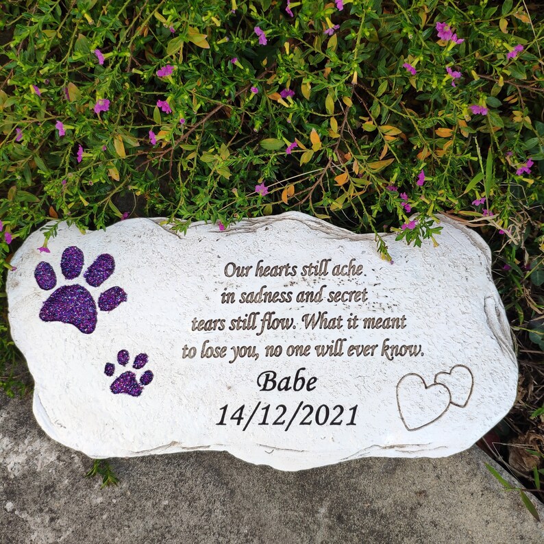 May include: A white stone memorial with purple glitter paw prints and the name "Babe" and date "14/12/2021". The inscription reads "Our hearts still ache in sadness and secret tears still flow. What it meant to lose you, no one will ever know."