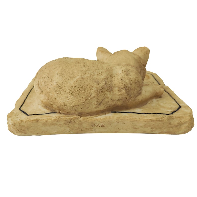 May include: A beige ceramic sculpture of a sleeping cat lying on a rectangular base with a black border. The base has a small inscription in Japanese.
