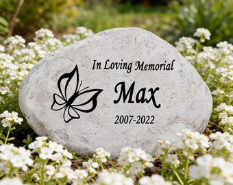 Può includere: Una pietra commemorativa grigio chiaro con una grafica a farfalla nera e il testo inciso In Loving Memorial, Max, e gli anni 2007-2022. La pietra ha una superficie naturale testurizzata ed è posizionata tra piccoli fiori bianchi.