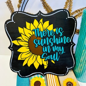 May include: Black wooden sign with a white border and a sunflower graphic. The sign reads "There is sunshine in my soul" in white and blue lettering.