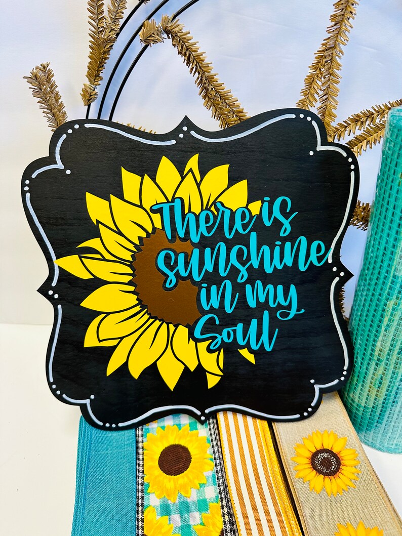 May include: Black wooden sign with a white border and a sunflower graphic. The sign reads "There is sunshine in my soul" in white and blue lettering.