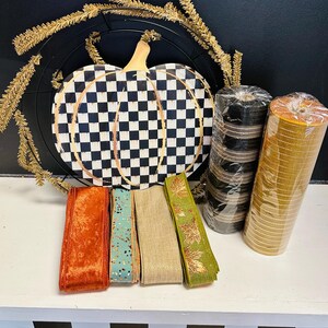 May include: A craft supply set featuring a black and white checkered pumpkin sign, a gold tinsel wreath frame, two rolls of mesh ribbon in black and gold, and four spools of ribbon in orange velvet, teal with gold flecks, tan, and green with gold leaves.