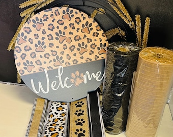 May include: A round wooden sign with a leopard print and paw prints, the word "Welcome" is written in white. Rolls of black and tan mesh, and patterned ribbons with paw prints and leopard print are also visible.