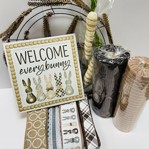 Peut inclure: Un assortiment de fournitures d'artisanat sur le th&egrave;me de P&acirc;ques. Comprend une enseigne avec l'inscription "WELCOME everybunny" avec des illustrations de lapins, des rouleaux de ruban, des carottes d&eacute;coratives et un cadre de couronne en m&eacute;tal. La palette de couleurs comprend du marron, du blanc et du beige.