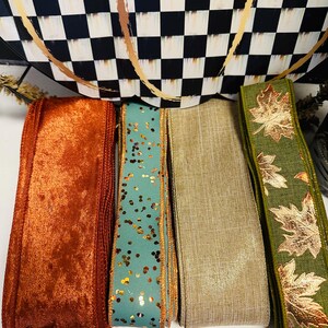 May include: Four rolls of decorative ribbon arranged side by side. The first is a textured burnt orange velvet, the second is a teal ribbon with gold glitter flecks, the third is a solid beige linen-like fabric, and the fourth is olive green with metallic gold maple leaf patterns.