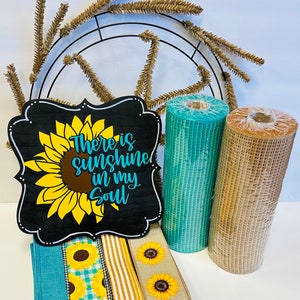 May include: A craft supply kit for making a sunflower wreath. The kit includes a metal wreath form, brown and teal mesh ribbon, sunflower patterned ribbon, and a wooden sign that reads "There is sunshine in my soul".