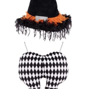 May include: A Halloween decoration featuring a black witch hat with orange trim and a black and white diamond-patterned body and legs. The legs have orange fringe and black shoes. The decoration is designed to hang.