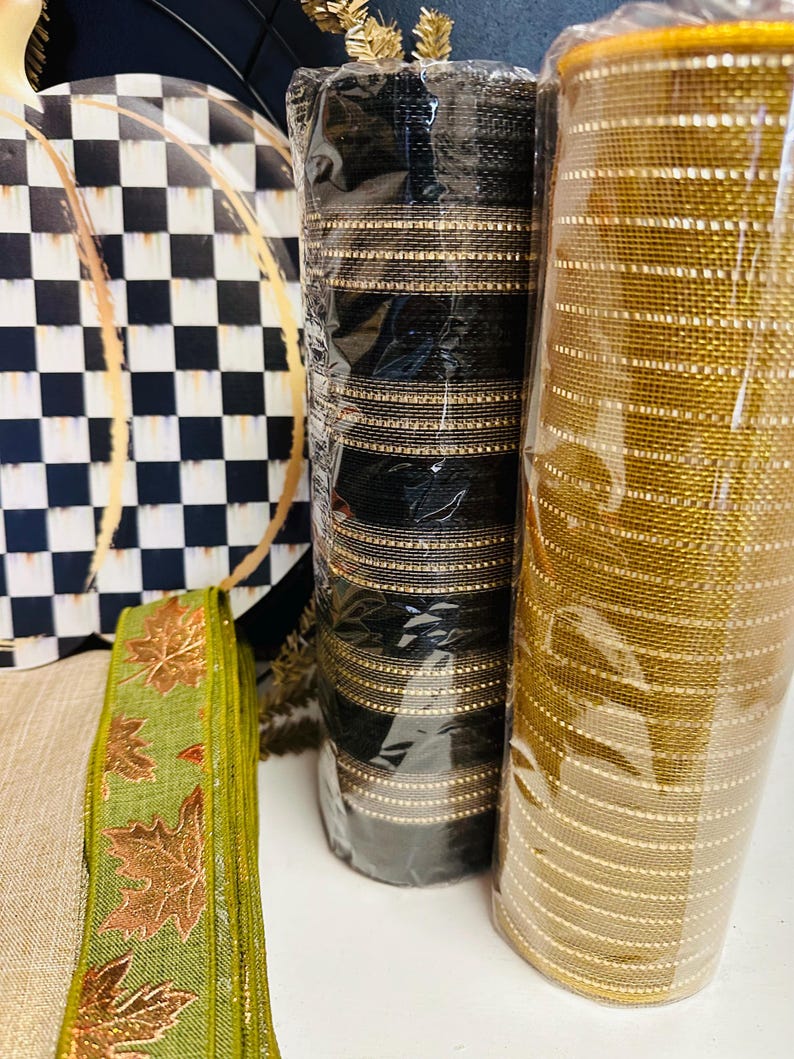 May include: Two rolls of mesh ribbon, one black with gold stripes and one solid gold, stand next to a green ribbon featuring a copper-colored leaf pattern and a round sign with a black and white checkered pattern and gold line accents.
