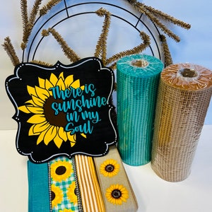 May include: A wooden sign with a sunflower and the text "There is sunshine in my soul". The sign is surrounded by teal and brown mesh ribbon, gold and white striped ribbon, and a teal and white gingham ribbon with sunflowers.